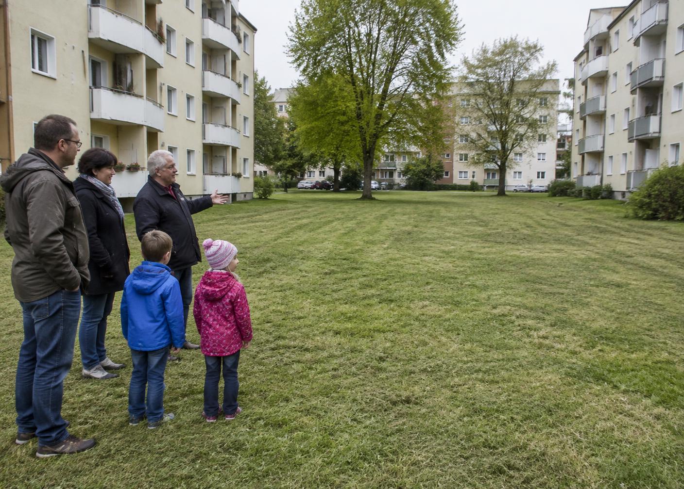 Nachbarinnen, Nachbarn und Kinder stehen vor einer kurz gemähten Rasenfläche im Wohnquartier und besprechen sie